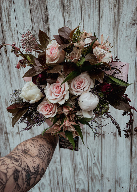 Bouquet of flowers held by a tattooed arm against a wooden background