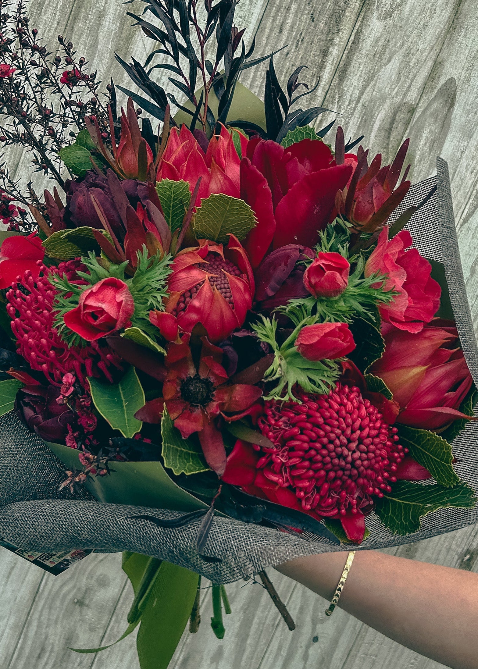 Bouquet of red flowers with green leaves on a wooden surface
